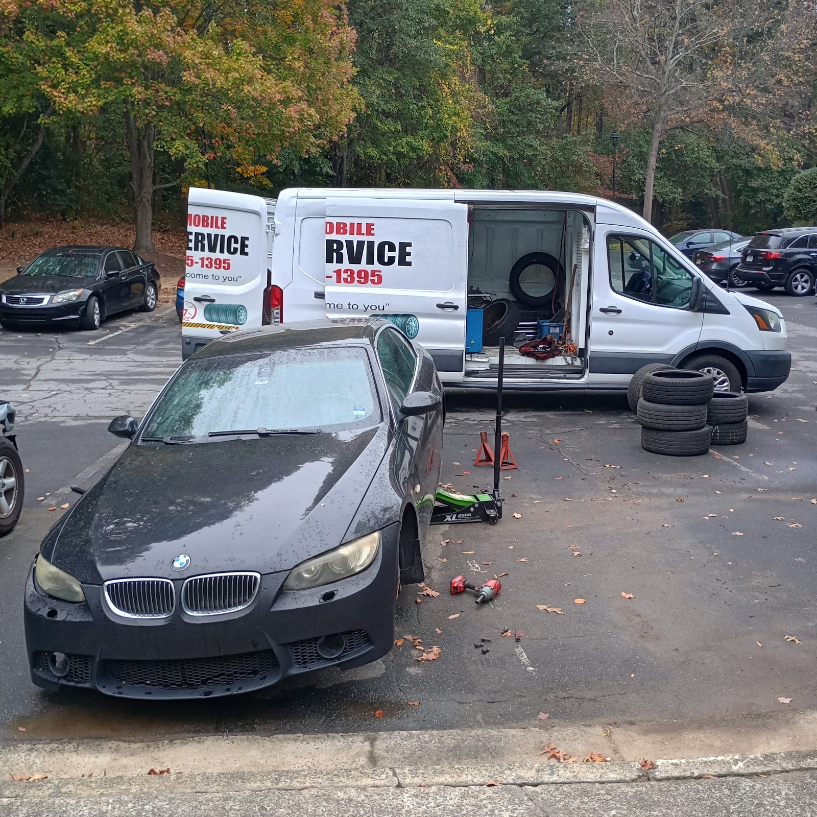 Zion Mobile Tire Services — branded mobile service van and new tires alongside a black BMW sedan mid-install